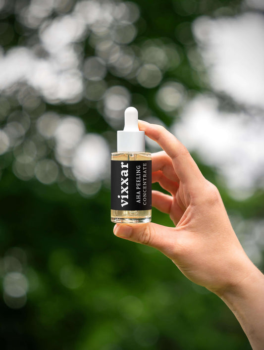 Person holding a 30ml AHA Peeling Concentrate with Lactic and Hyaluronic Acid against an outdoor blurred background.