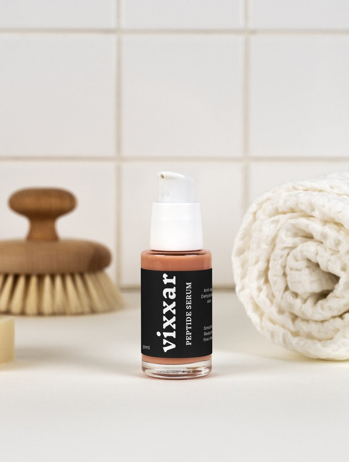 Bottle of Vixxar peptide serum on a bathroom counter with a towel and brush in the background.