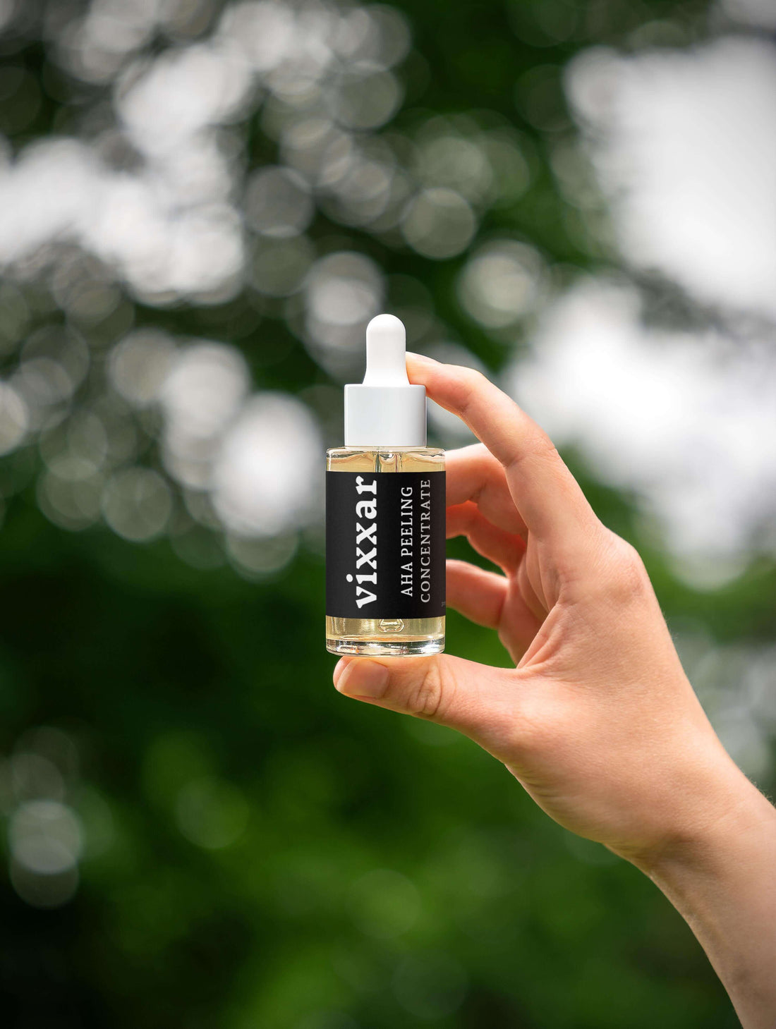 Person holding a 30ml AHA Peeling Concentrate with Lactic and Hyaluronic Acid against an outdoor blurred background.